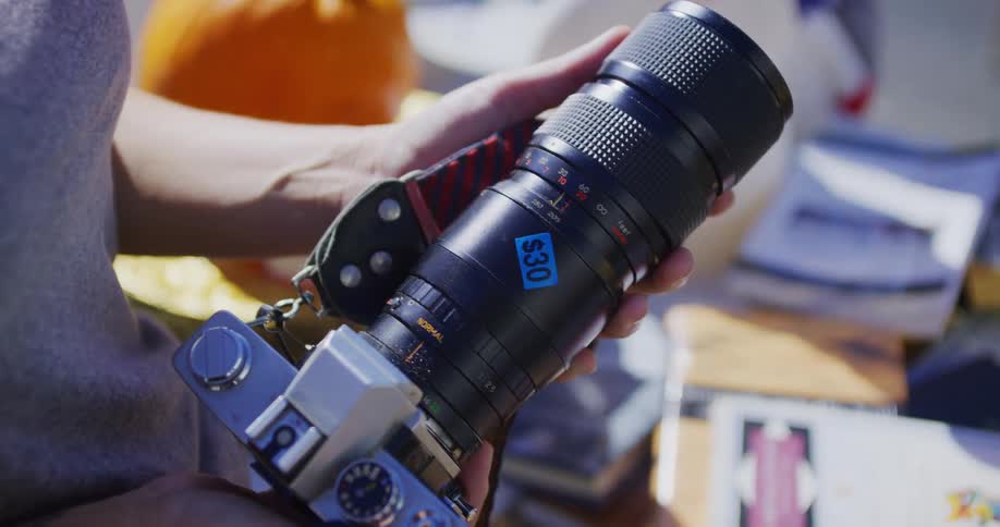 A person stands outdoors on a sunny day holding a digital camera with a large lens ready to capture the scene