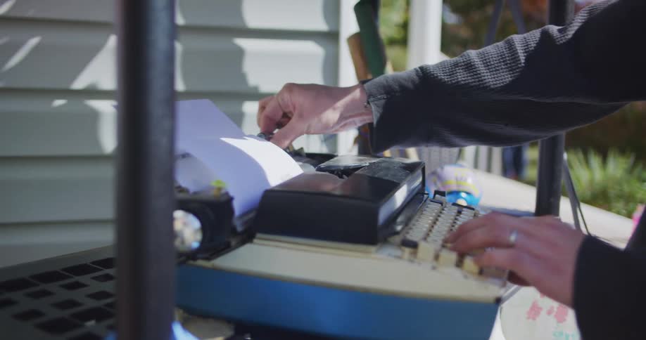 A person struggles to adjust the paper on a vintage typewriter and gestures in frustration when it malfunctions