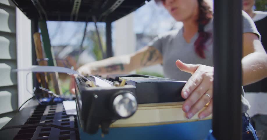 Man watches while a woman tests a typewriter standing on a shelving unit outdoors on an autumn day
