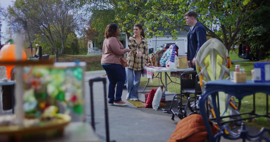 People talk beside tables with items displayed at a garage sale