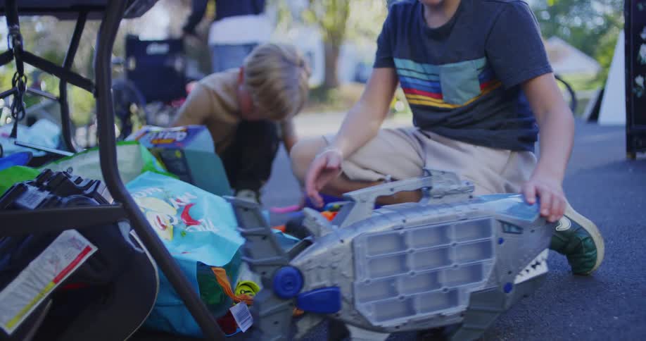 As a person walks by on a driveway two boys play with toys on a driveway happily
