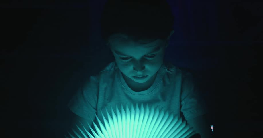Child looks at a glowing bookshaped lamp in a dark room