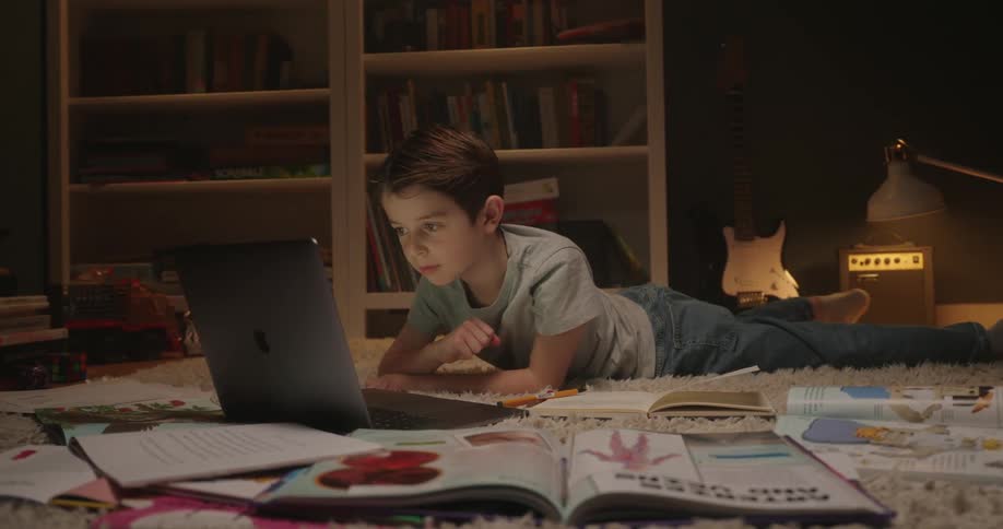 A boy using a laptop while laying on the ground