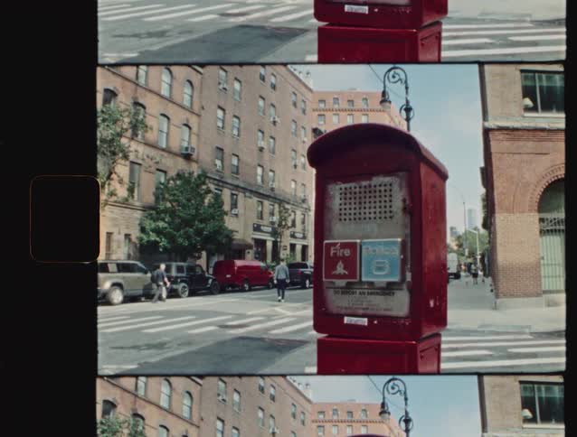 Emergency services call box stands near an intersection as people cross the street