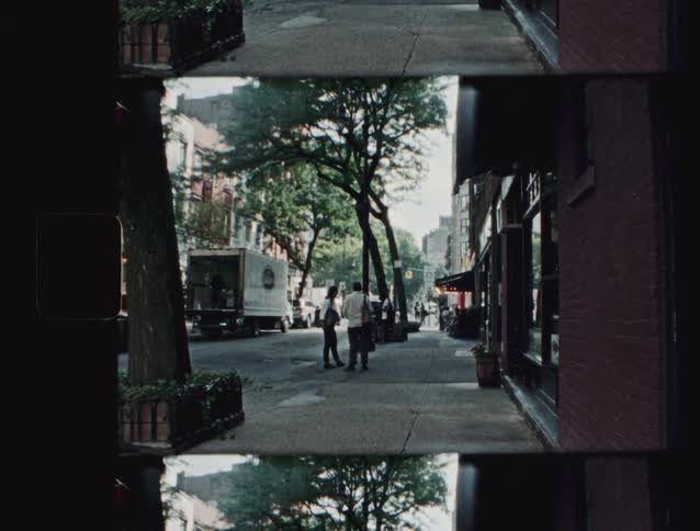 People talk on a treelined sidewalk while a truck is parked on the street