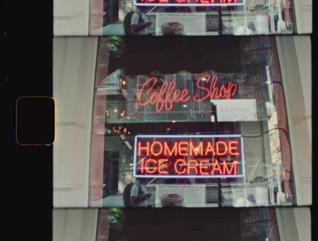 Neon signs reading coffee shop and homemade ice cream illuminate a storefront window on a city street filmed on 16mm film stock