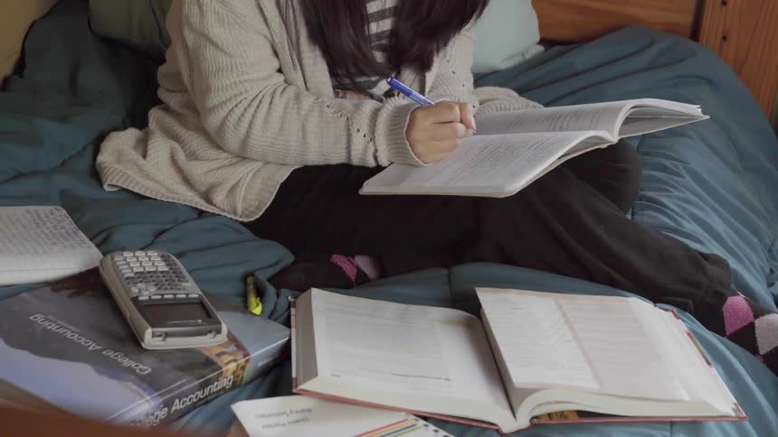 Teenager does homework while sitting on a bed
