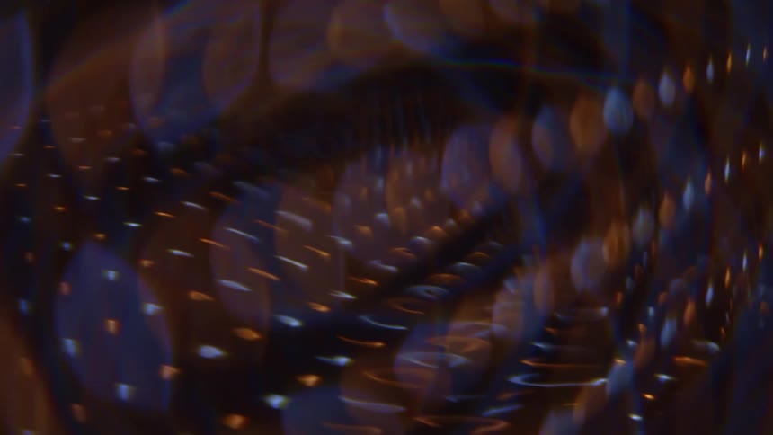 This is a video of an abstract dark background with rotating swirling light effects and bokehthe lights consist of horizontal dashed lines of gold and bluewhite colors that appear to be moving in a circular or spiral pattern creating a feeling of