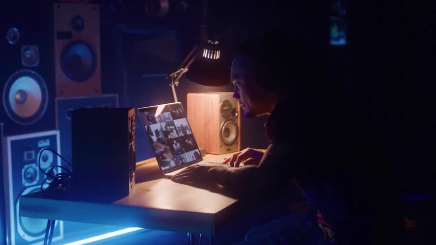 Man sitting in a room containing a wall of speakers leans forward to focus on a laptop with pictures