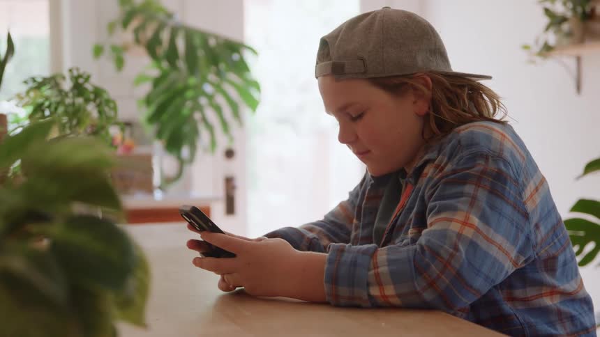 Young boy sitting at a table texting on his phone