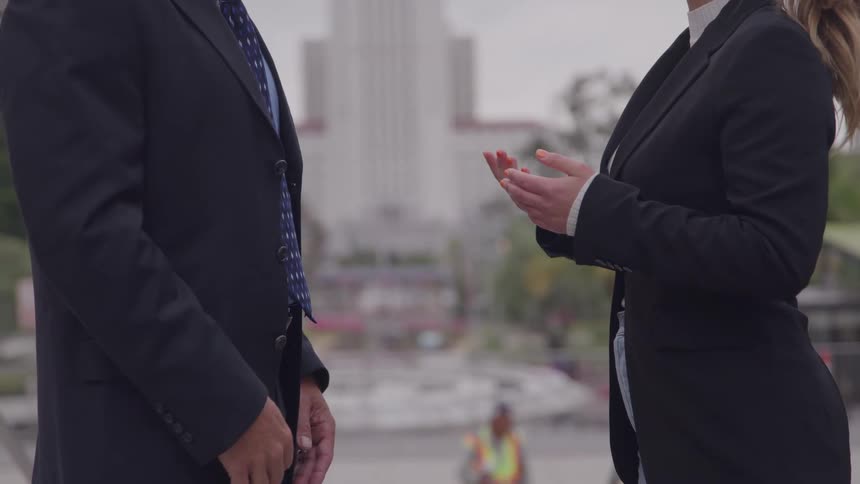 Man and woman facing each other and move their hands as the talk outside of downtown buildings