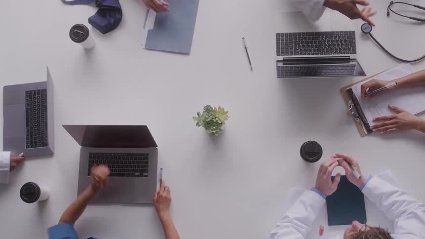 Plant in the center of a table as people set down their laptop computers and clipboards and start working typing and writing