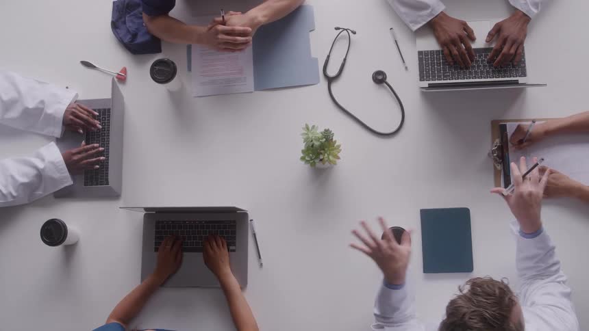 Medical professionals collaborate around a table with laptops and notes