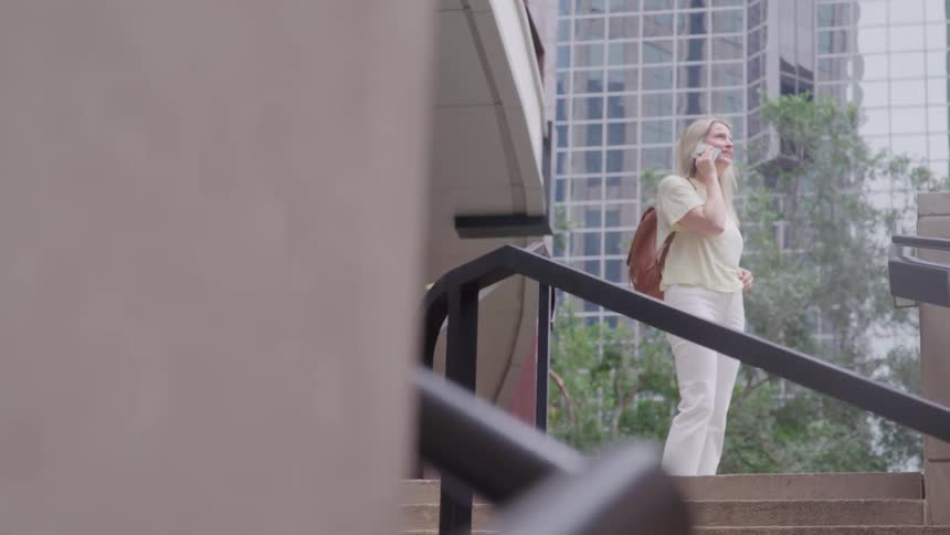 A young woman talks on her phone while standing on a staircase in the city