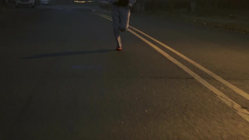Person running down a two-lane road at night as seen from their waist down