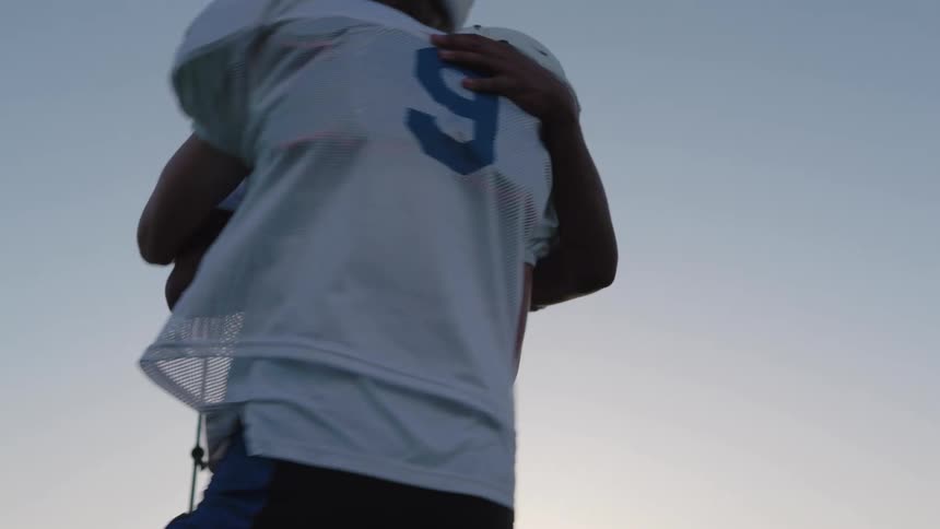 Two football players exchange a low five beneath stadium lights against the evening sky