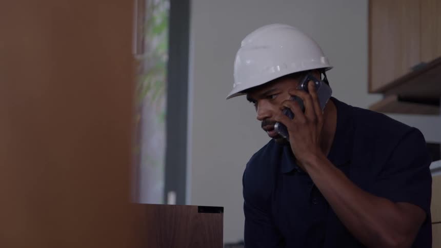 Utility worker stands inside a house talking on the phone