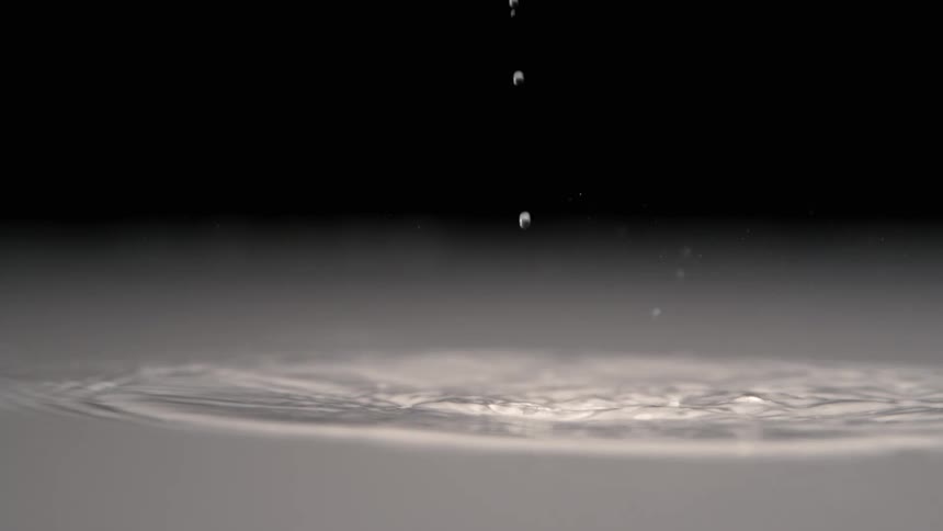 Droplets fall onto a liquid surface creating a visible splash