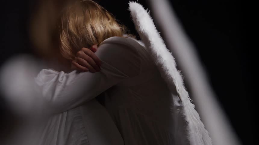 Person with white wings hugging their knees in a dark setting