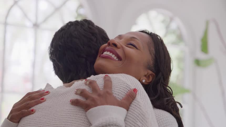 Close up portrait of two black women hugging each other while standing in a white hall during daytime