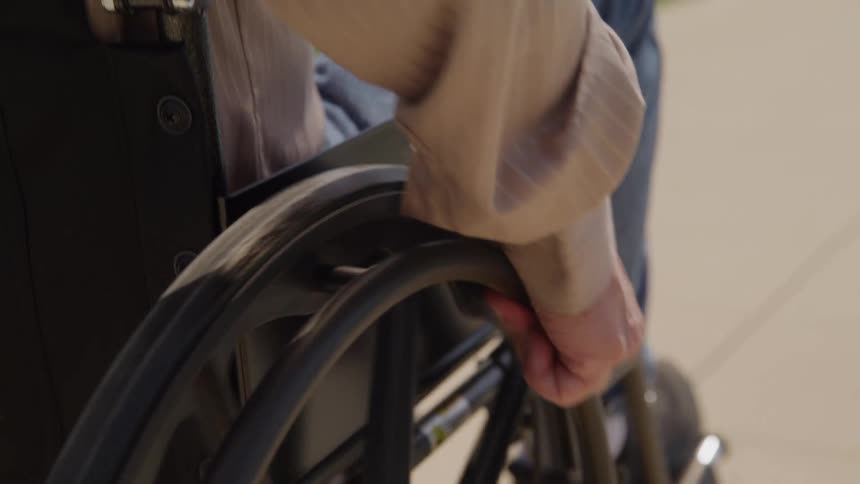 Man wheels his wheelchair along the sidewalk during the daytime