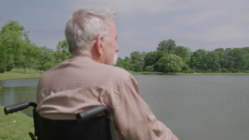 Man in a wheelchair faces the lake in a wooded area
