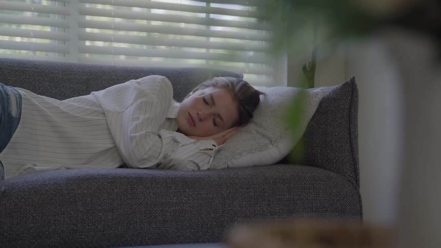 Woman lying on a couch sleeps with her head resting on a pillow