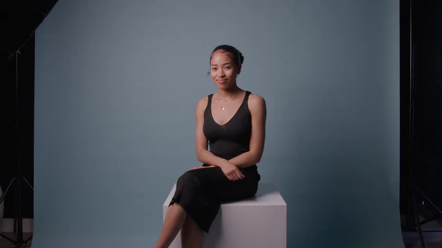 Woman sits calmly against blue backdrop in studio with visible lighting equipment