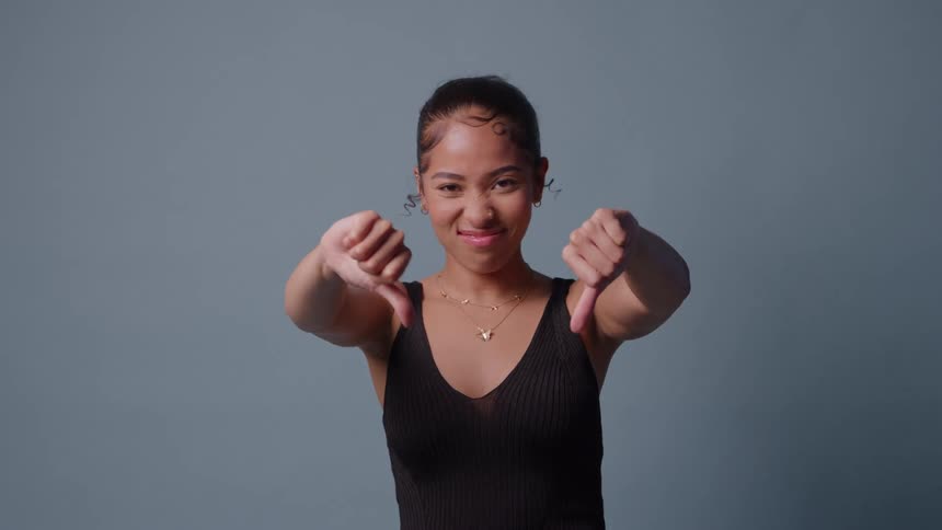 Woman makes thumbsdown gesture against light blue background