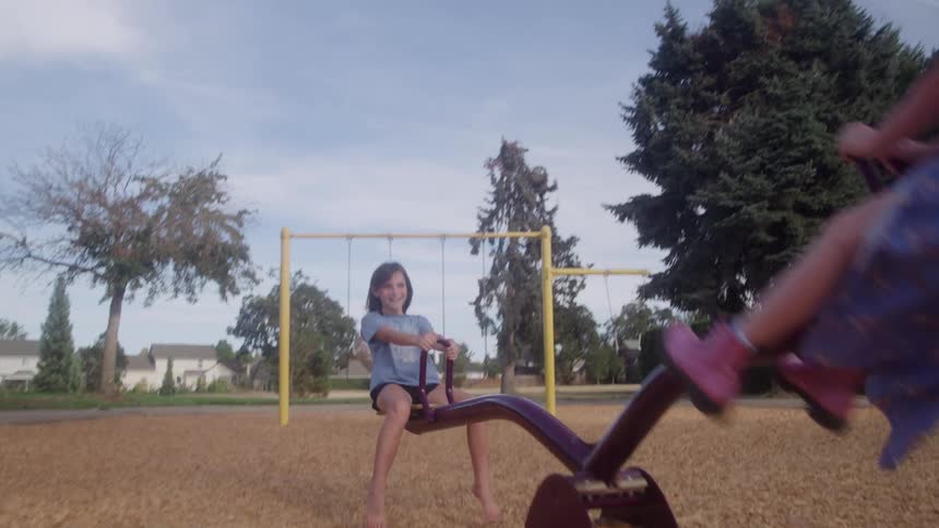 Two girls riding on a seesaw in a neighborhood park