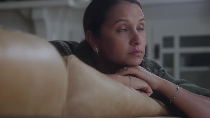 Woman rests chin on folded hands in a serene moment atop light leather surface
