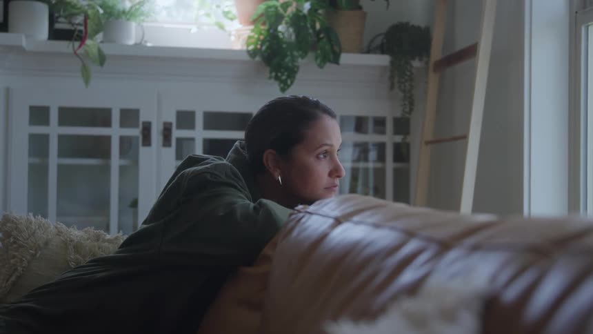 The woman sits on the couch while looking out the window