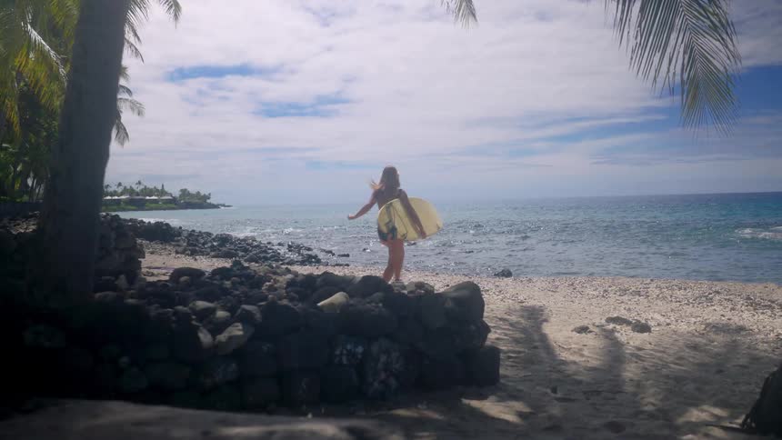 Woman walks along the sand with a surfboard toward the sea