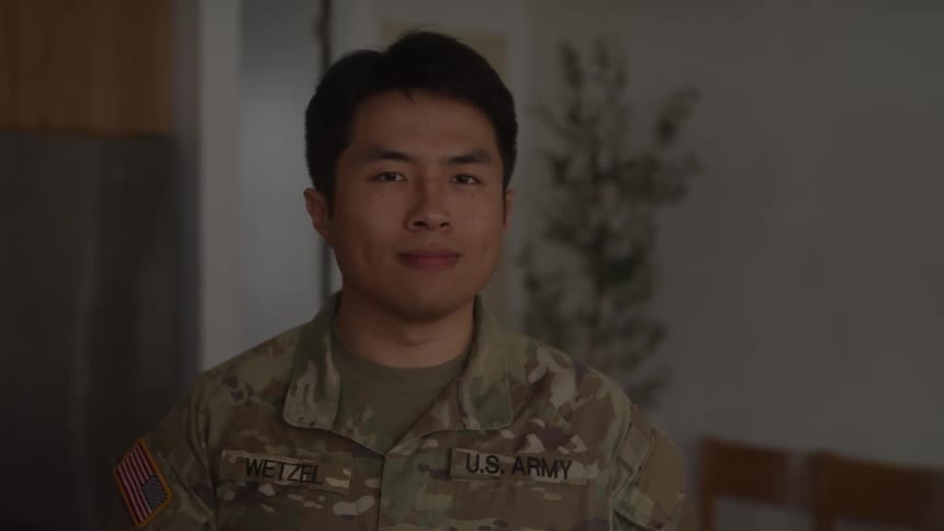 Us army service member in camouflage uniform stands indoors with a plant in the background