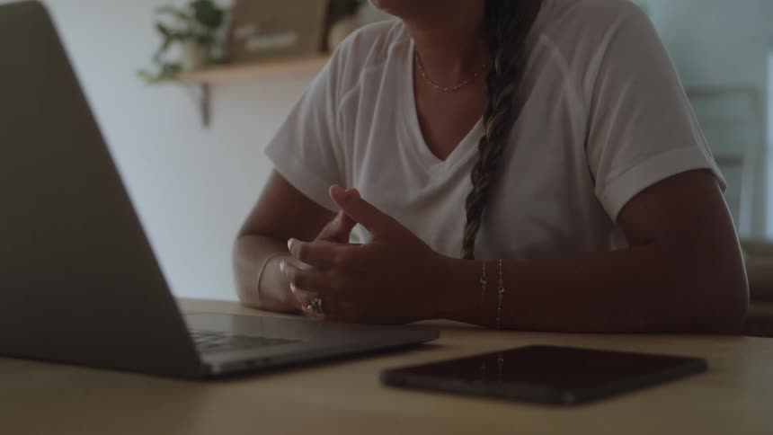 Woman with braid gestures in front of laptop on wooden table