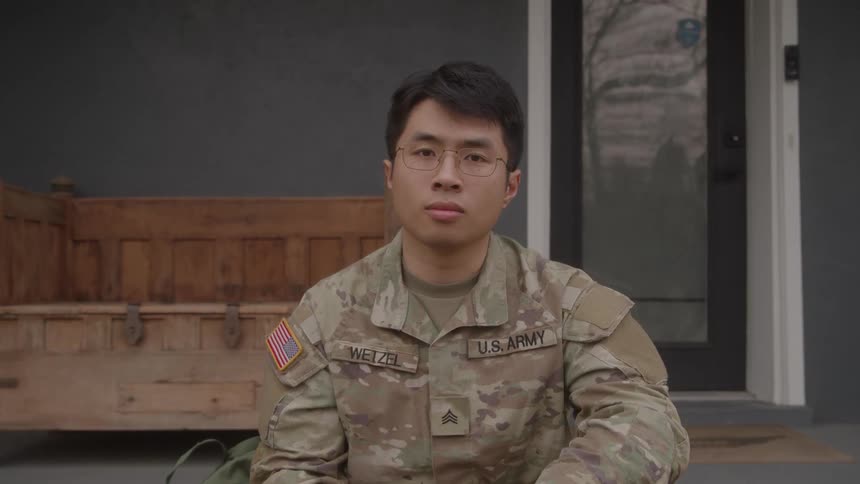 Us army service member with glasses and uniform sits in front of wooden bench on porch
