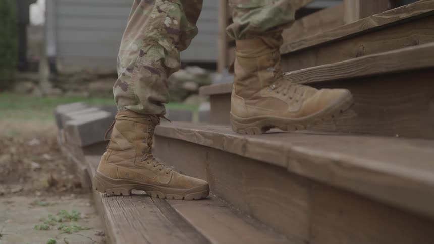 Soldier wearing camouflage fatigues walks up the front steps of a house