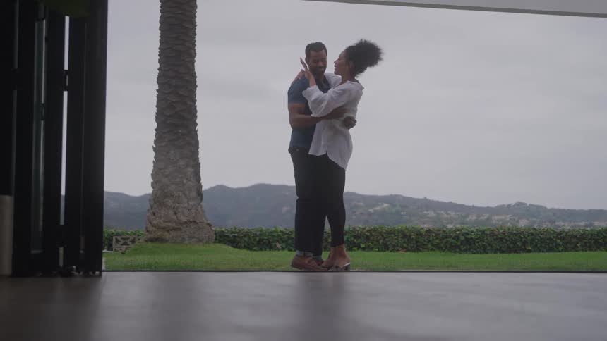 Couple looks at ring together on terrace overlooking hills and greenery under cloudy sky