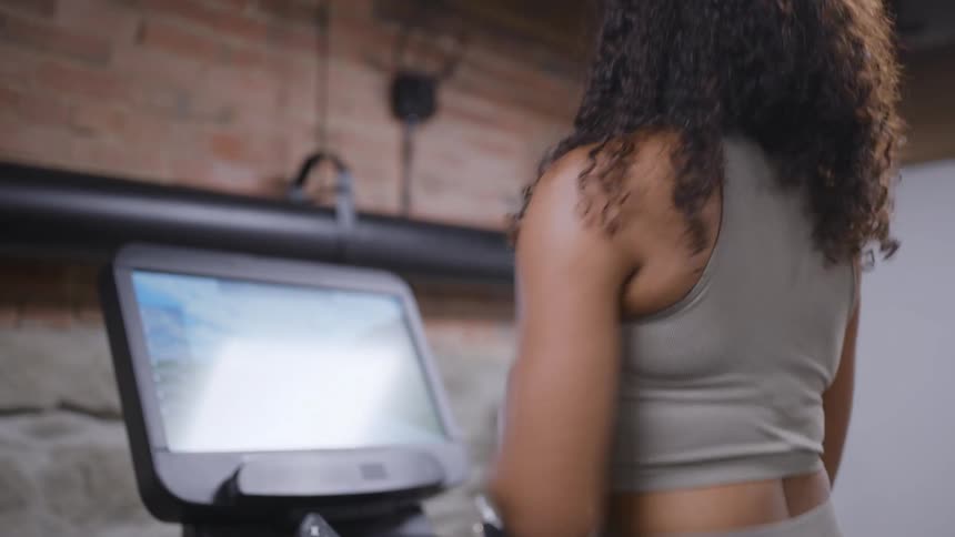 Woman runs on treadmill in gym with brick wall and visible digital screen