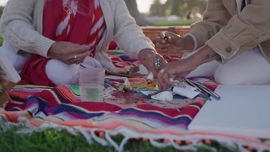 Two people arranging painting supplies on a colorful blanket
