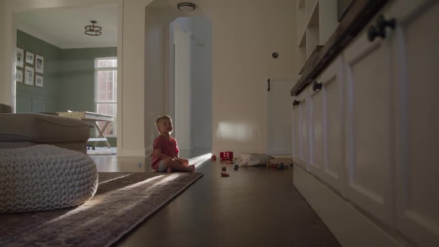 Child sitting on the floor among colorful toys with sunlight streaming through the doorway