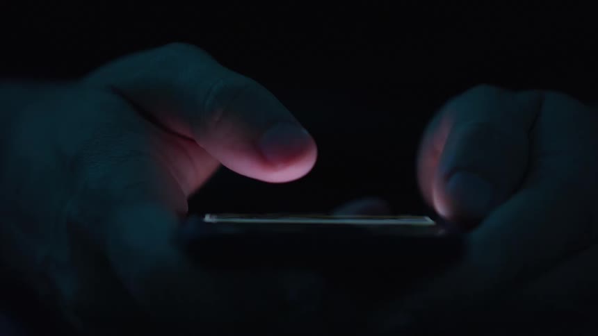 Man holding his phone and scrolling in the dark
