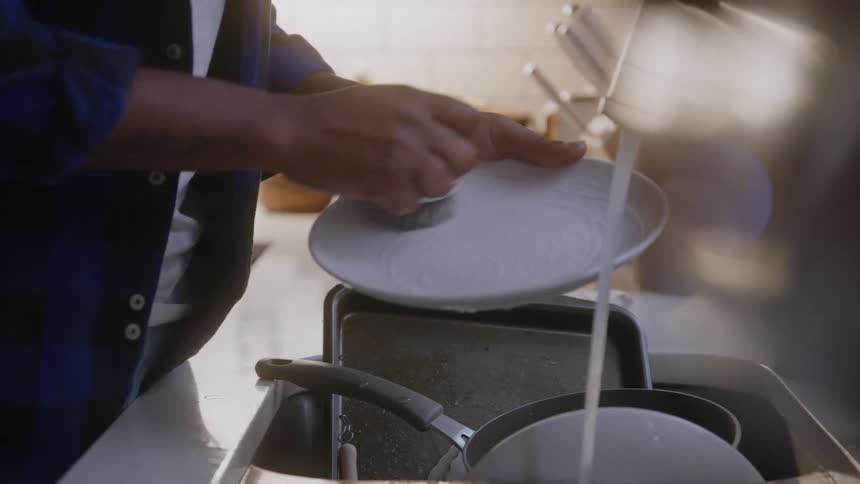 Hands washing a plate in a kitchen sink