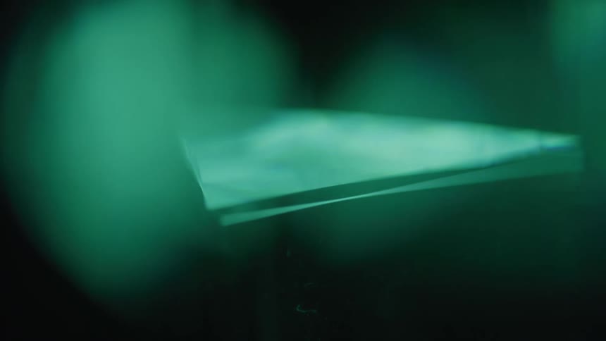 An abstract view of a prism with sharp edges rotating in a dark setting generating a teal and green color shift effect