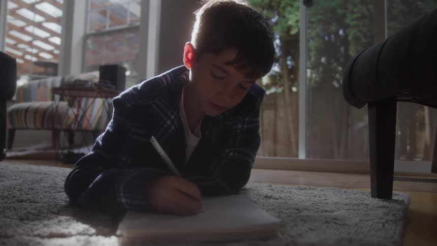 Boy lying on the rug drawing in a notebook