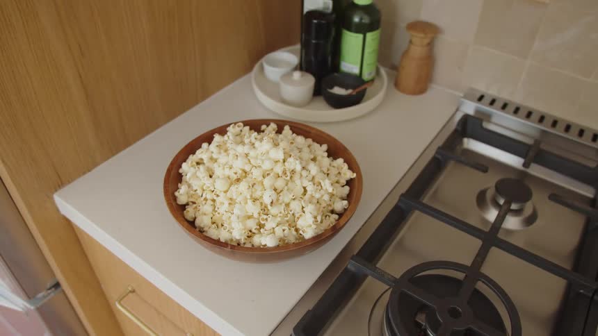 Bowl of popcorn sits on the counter beside the stove and seasonings