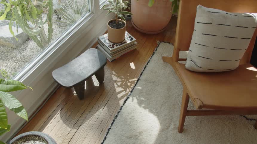 A high angle close view of a contemporary interior showing a leather chair a black wooden stool and potted plants next to a large window overlooking a rock garden