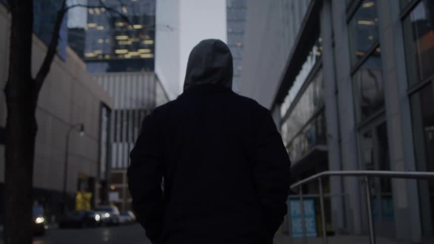 Man wearing a hooded jacket walks on a downtown sidewalk