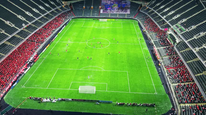 An aerial view pans across a brightly lit soccer stadium at night capturing the dynamic movement of players on the field as fans fill the surrounding stands