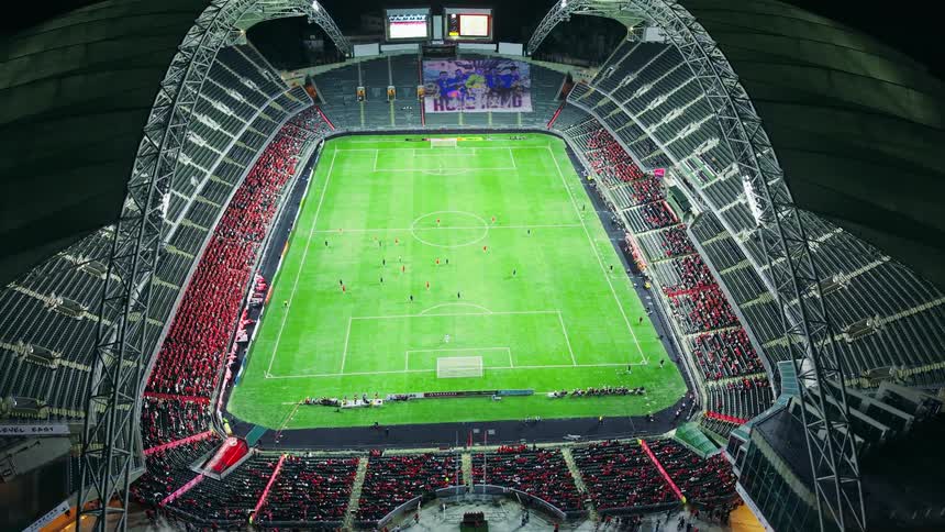 Soccer fans sit in a brightly lit stadium at night
